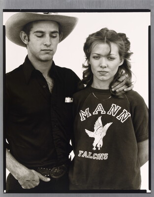 A black-and-white portrait photograph of a young White man wearing a cowboy hat, looking down, his hand affectionately around the neck of a young White woman.