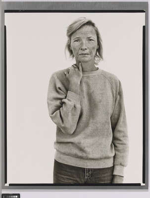 A black-and-white portrait photograph of a tired-looking White woman wearing a sweatshirt and holding her hand on her shoulder as if it might ache.