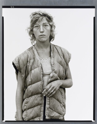A black-and-white portrait photograph of a young White woman with short wavy hair wearing a puffer vest looking straight at the viewer.