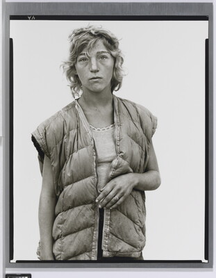 A black-and-white portrait photograph of a young White woman with short wavy hair wearing a puffer vest looking straight at the viewer.