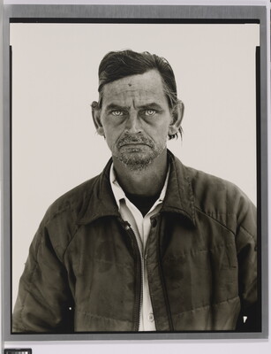 A black-and-white portrait photograph of a White man with a salt-and-pepper goatee wearing a collared shirt under a quilted jacket.