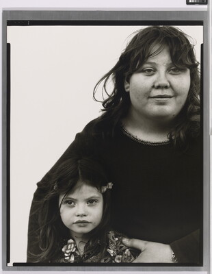 A black-and-white portrait photograph of a medium-skinned woman with dark hair holding close to her a young medium-skinned girl with long dark hair in barrettes.