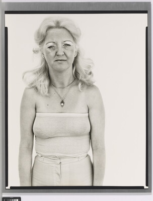 A black-and-white portrait photograph of a White woman with long, bleach-blonde hair in a white tube top and pants.