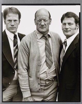 A black-and-white portrait photograph of three White men, two younger on the left and right and the one in the center middle-aged and bald, all wearing suits and ties.