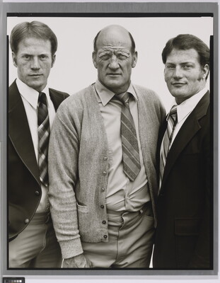 A black-and-white portrait photograph of three White men, two younger on the left and right and the one in the center middle-aged and bald, all wearing suits and ties.