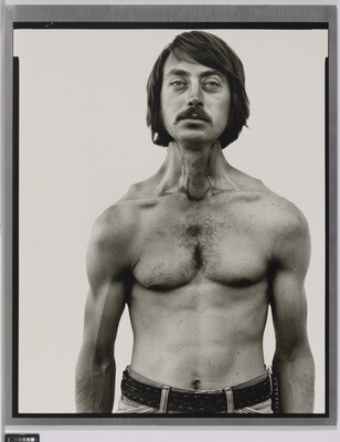 A black-and-white portrait photograph of a shirtless White man, with dark hair and a mustache, and thin but with muscled shoulders and arms.