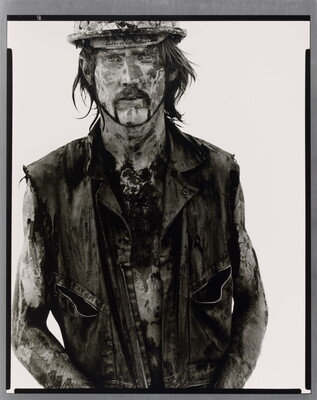 A black-and-white portrait photograph of a White man covered in dirt and oil wearing a vest and hard hat.