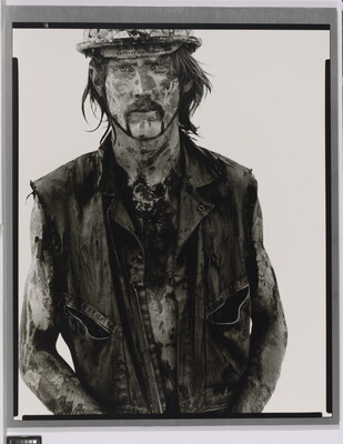A black-and-white portrait photograph of a White man covered in dirt and oil wearing a vest and hard hat.