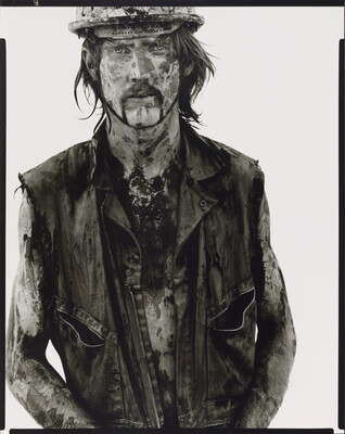 A black-and-white portrait photograph of a White man covered in dirt and oil wearing a vest and hard hat.