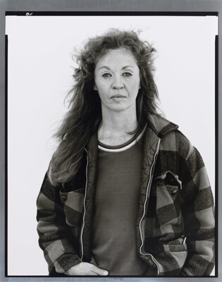 A black-and-white portrait photograph of a middle-aged White woman with long hair wearing a checked jacket.