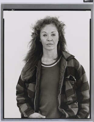 A black-and-white portrait photograph of a middle-aged White woman with long hair wearing a checked jacket.