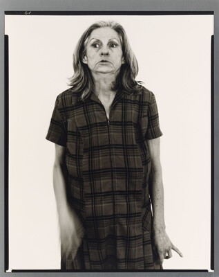 A black-and-white portrait photograph of an older White woman with medium-length gray hair, head held back slightly, wearing a house dress.