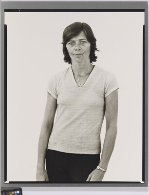 A black-and-white portrait photograph of a White woman with short hair, wearing a light V-neck shirt and dark pants.