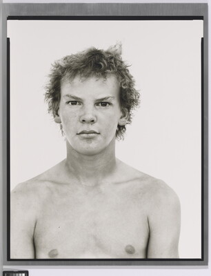 A black-and-white portrait photograph of a shirtless White teenage boy with messy hair.