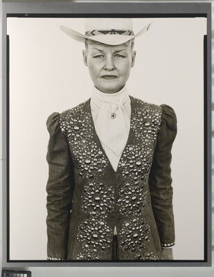 A black-and-white portrait photograph of a White woman wearing a white cowboy hat and a jacket embellished with rhinestones in a floral pattern over a white blouse.