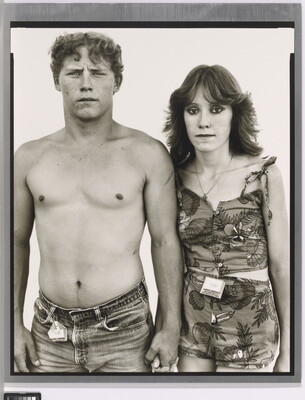 A black-and-white portrait photograph of a young, shirtless White man holding hands with a young White woman wearing a tank top and shorts.
