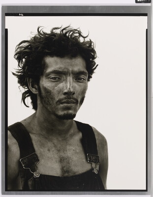 A black-and-white portrait photograph of a man from the chest up with messy hair, a dirty face, and overalls.