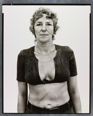 A black-and-white portrait photograph of a White woman with short, curly hair wearing a cropped shirt with a very low neckline.