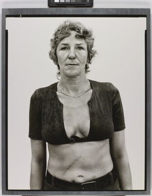 A black-and-white portrait photograph of a White woman with short, curly hair wearing a cropped shirt with a very low neckline.