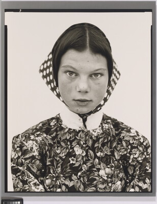 A black-and-white portrait photograph of a teenage White girl wearing a high-collared, floral print blouse and a polka-dotted head scarf.