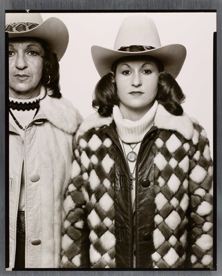 A black-and-white portrait photograph of two White women standing shoulder-to-shoulder; both wear cowboy hats and coats with fur collars.