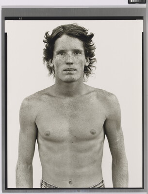 A black-and-white portrait photograph of a shirtless young White man with freckles across his face and shoulders.
