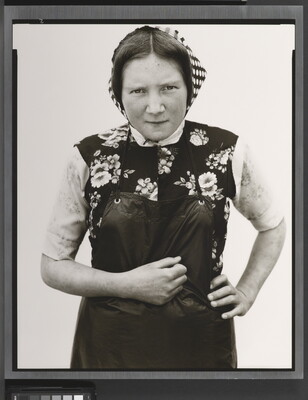 A black-and-white portrait photograph of young White woman wearing a checked kerchief, flowered vest, and dark apron.