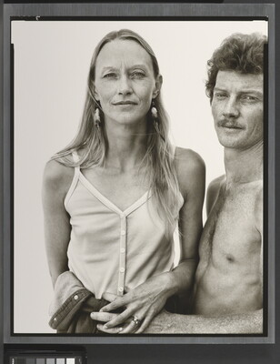 A black-and-white portrait photograph of a thin White woman with long hair wearing camisole as a shirtless White man with curly hair and a moustache holds her waist.