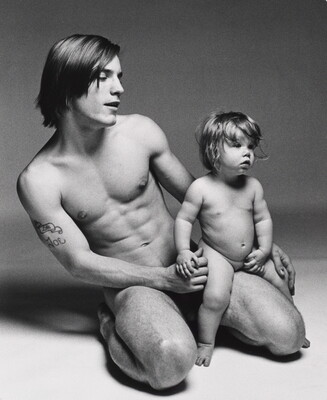 A black-and-white photograph of a nude White man kneeling and holding a nude White toddler on his knee.
