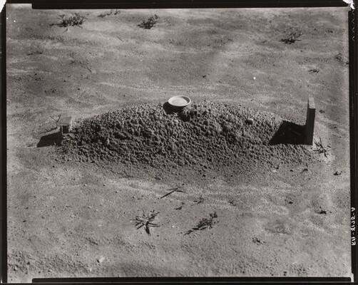 A black-and-white photograph of a freshly dug grave and headstone in a barren landscape.