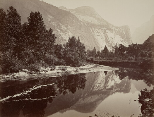 A black-and-white photograph of a mountain landscape with a river in the foreground reflecting the trees and mountain.
