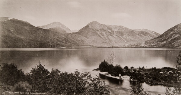 A black-and-white photograph of a lake surrounded by mountains.