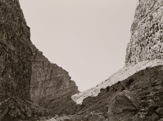 A black-and-white photograph of steep and rocky cliffs rising on both sides of a rocky valley.