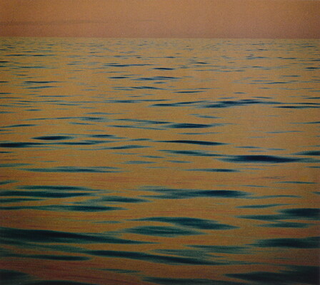 A color photograph of calm ripples of the sea at sunset reflecting an orange-red sky.