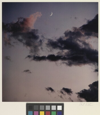 A color photograph of a blue-gray sky, dark clouds, and a crescent moon.