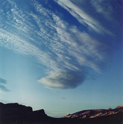 A color photograph of radiatus white clouds in a blue sky over a rocky landscape.