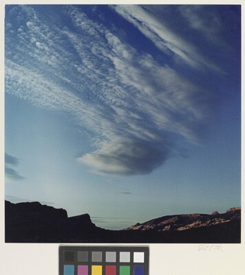 A color photograph of radiatus white clouds in a blue sky over a rocky landscape.
