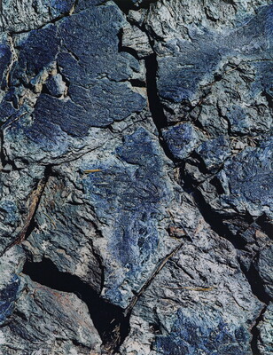 A color close-up photograph of a rough blue-tinged rock with cracks.