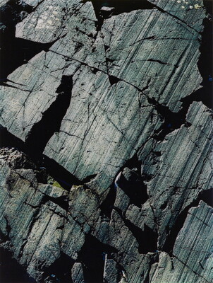 A color close-up photograph of dark gray rocks with diagonal striations and cracks.