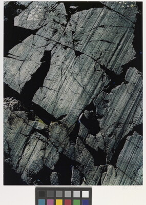 A color close-up photograph of dark gray rocks with diagonal striations and cracks.