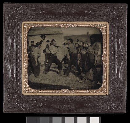 A framed black-and-white photograph of two men pretending to fight surrounded by other men who are watching.