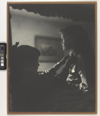 A black-and-white photograph of two young White girls, one fastening a ribbon around the neck of the other, both in shadow.