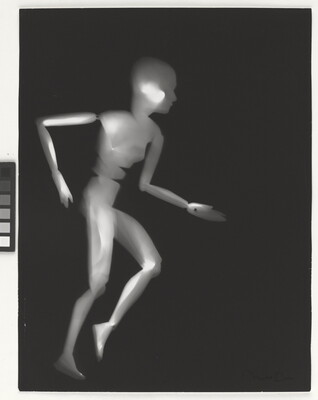 A black-and-white photograph of a white person-shaped puppet running on a black background.