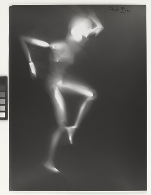 A black-and-white photograph of a white person-shaped puppet dancing on a black background.
