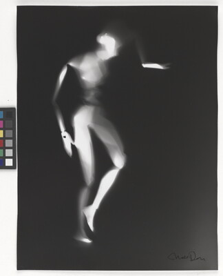 A black-and-white photograph of a white person-shaped puppet dancing on a black background.