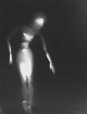 A black-and-white photograph of a white person-shaped puppet dancing on a black background.