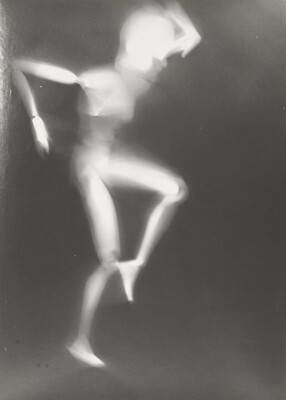 A black-and-white photograph of a white person-shaped puppet dancing on a black background.