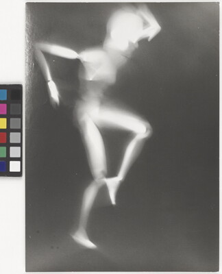 A black-and-white photograph of a white person-shaped puppet dancing on a black background.