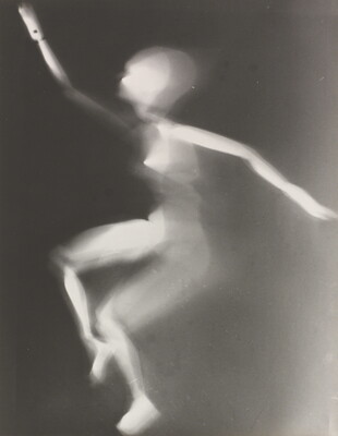 A black-and-white photograph of a white person-shaped puppet dancing on a black background.
