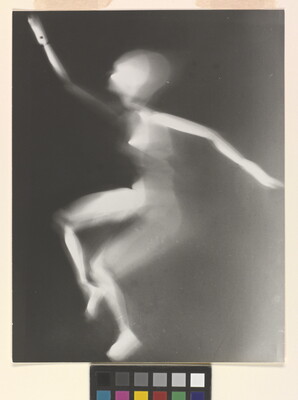 A black-and-white photograph of a white person-shaped puppet dancing on a black background.